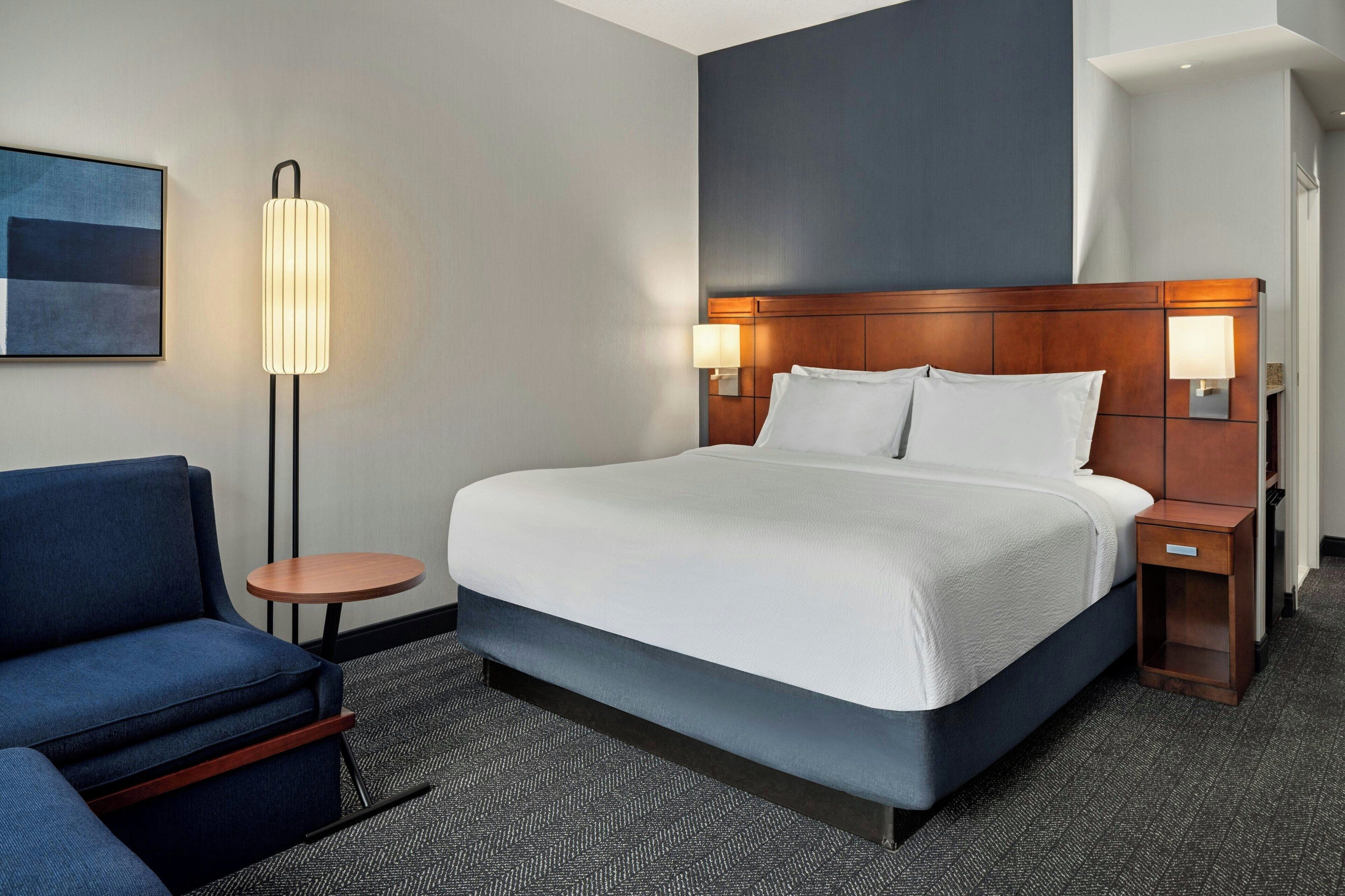 Une chambre d’hôtel avec un grand lit, un canapé bleu, une petite table ronde et deux lampes de chevet.