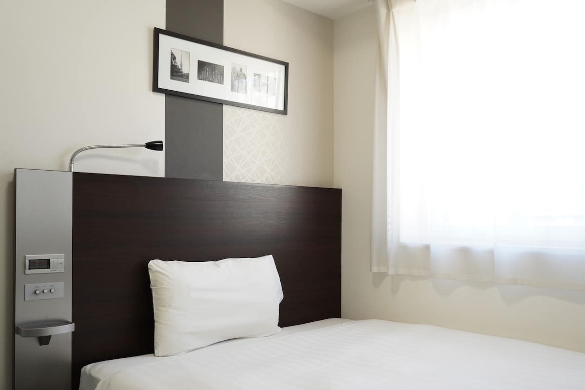 A hotel room with a bed, a headboard, a wall-mounted control panel, and a framed picture above the bed.