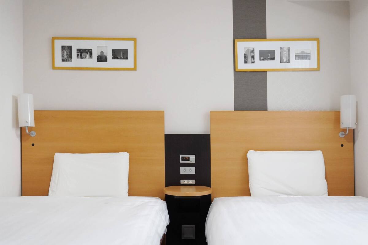 A hotel room with two beds, a nightstand, and a wall-mounted control panel.