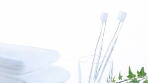 A glass with two toothbrushes and a stack of white towels. - Comfort Hotel Tokyo Kanda (Tokyo)