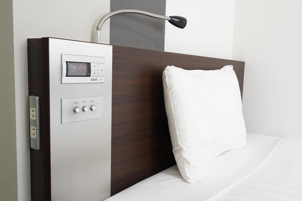 A modern hotel room with a control panel, a white pillow, and a headboard.