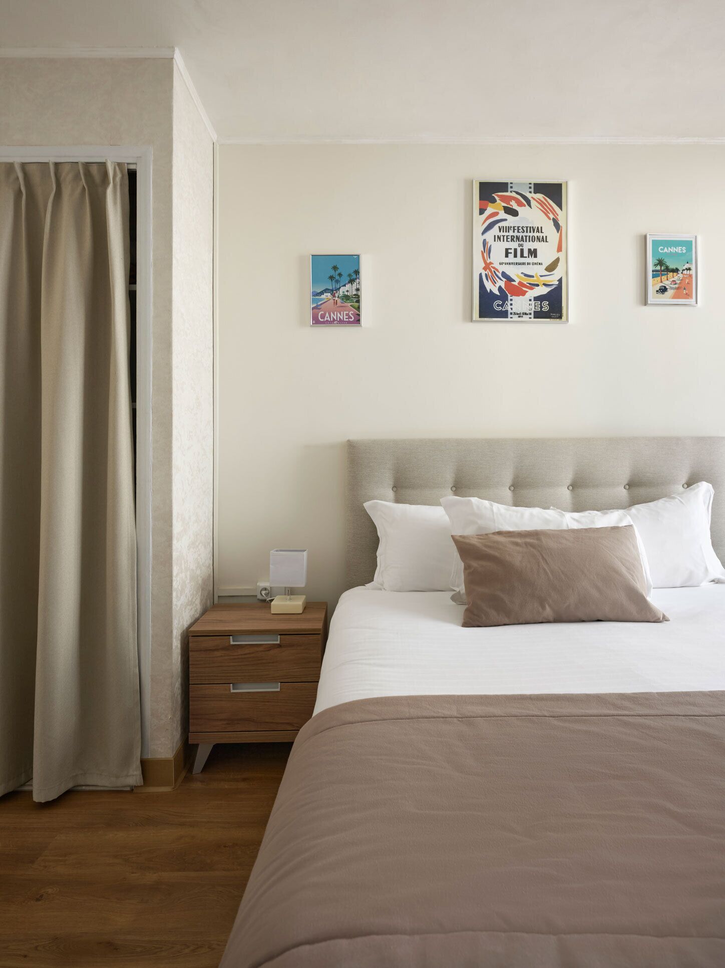 A neatly arranged bedroom with a bed, a bedside table, and a nightstand. There are two posters on the wall, one of which is a film festival poster.