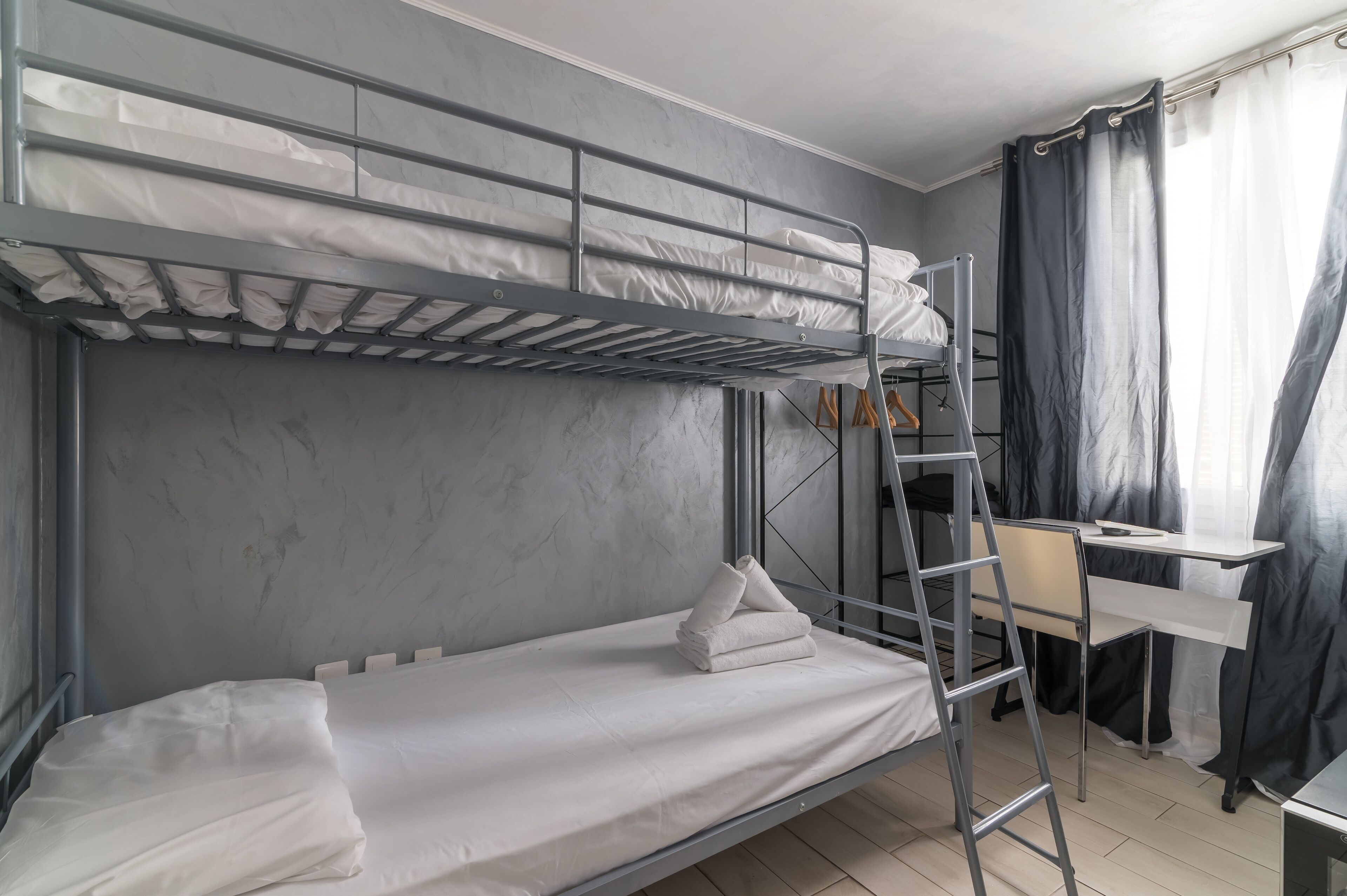 A bunk bed with a desk and chair, a ladder, and a window with curtains.