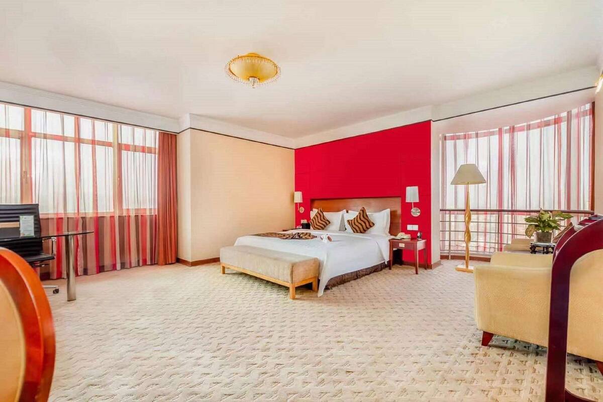 A hotel room with a large bed, a desk, a chair, and a window with curtains.
