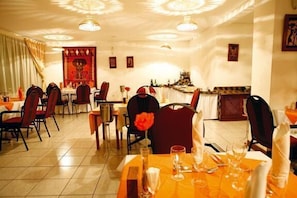 A dining area with multiple tables and chairs, a decorative wall, and a ceiling with circular light fixtures. - Lichinga Hotel by Montebelo (Lichinga)