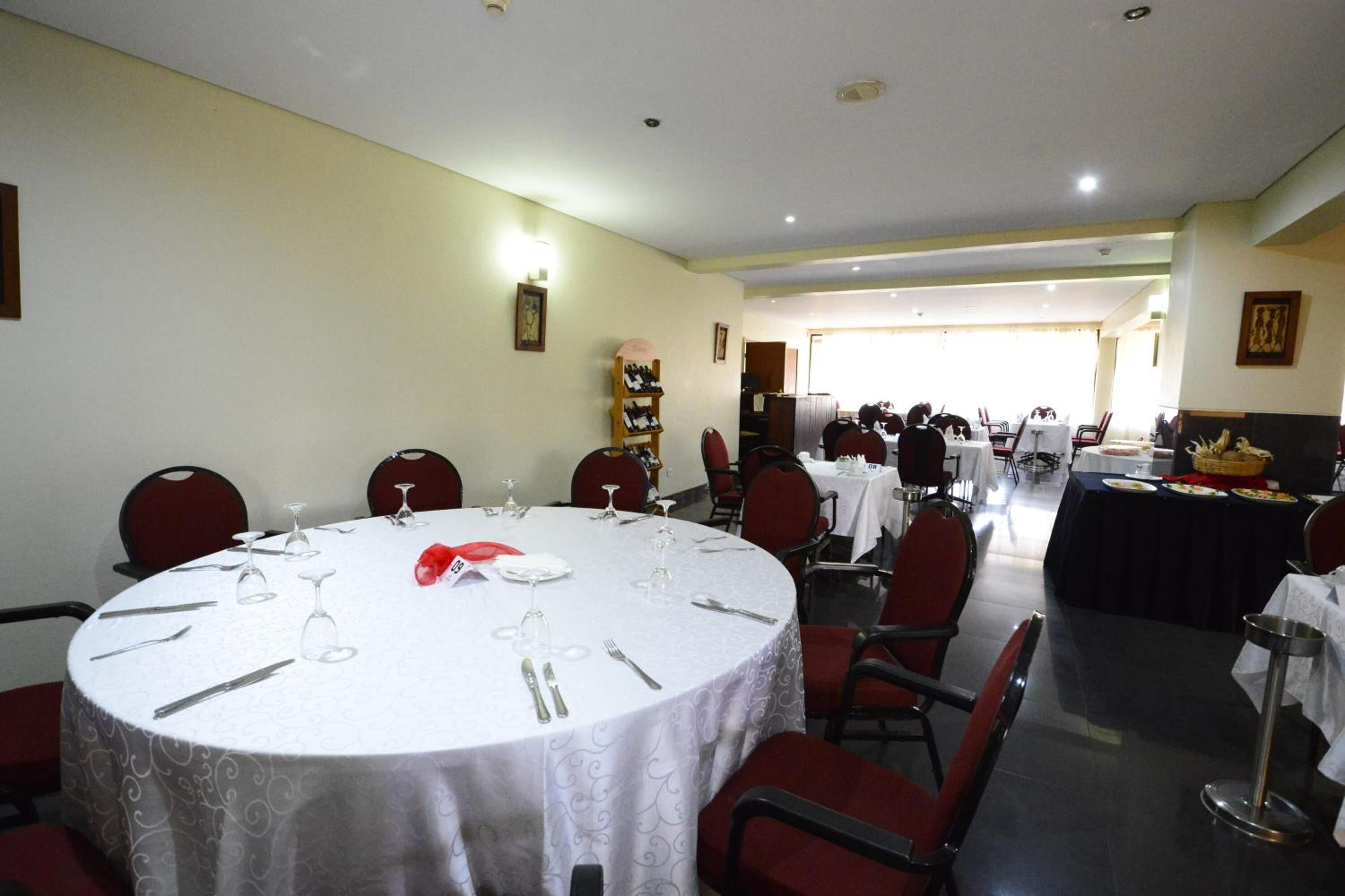 A dining area with round tables set for a meal, chairs, and a buffet table in the background.