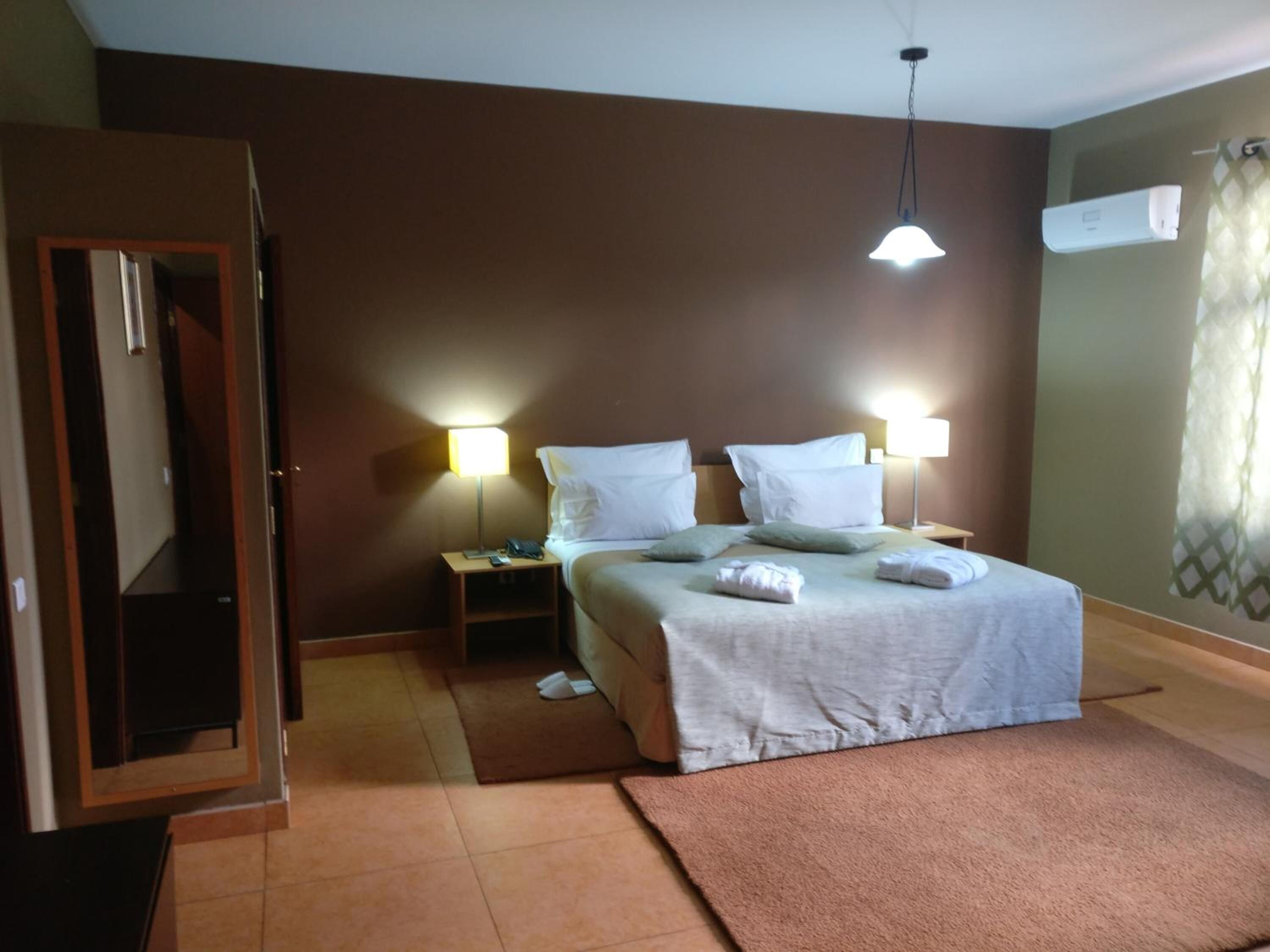 A hotel room with a bed, bedside lamps, a mirror, and a door.
