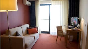 A hotel room with a sofa, a desk with a computer, a TV, and a lamp.