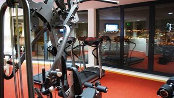 A gym with exercise equipment, a treadmill, and a large window with a city view.