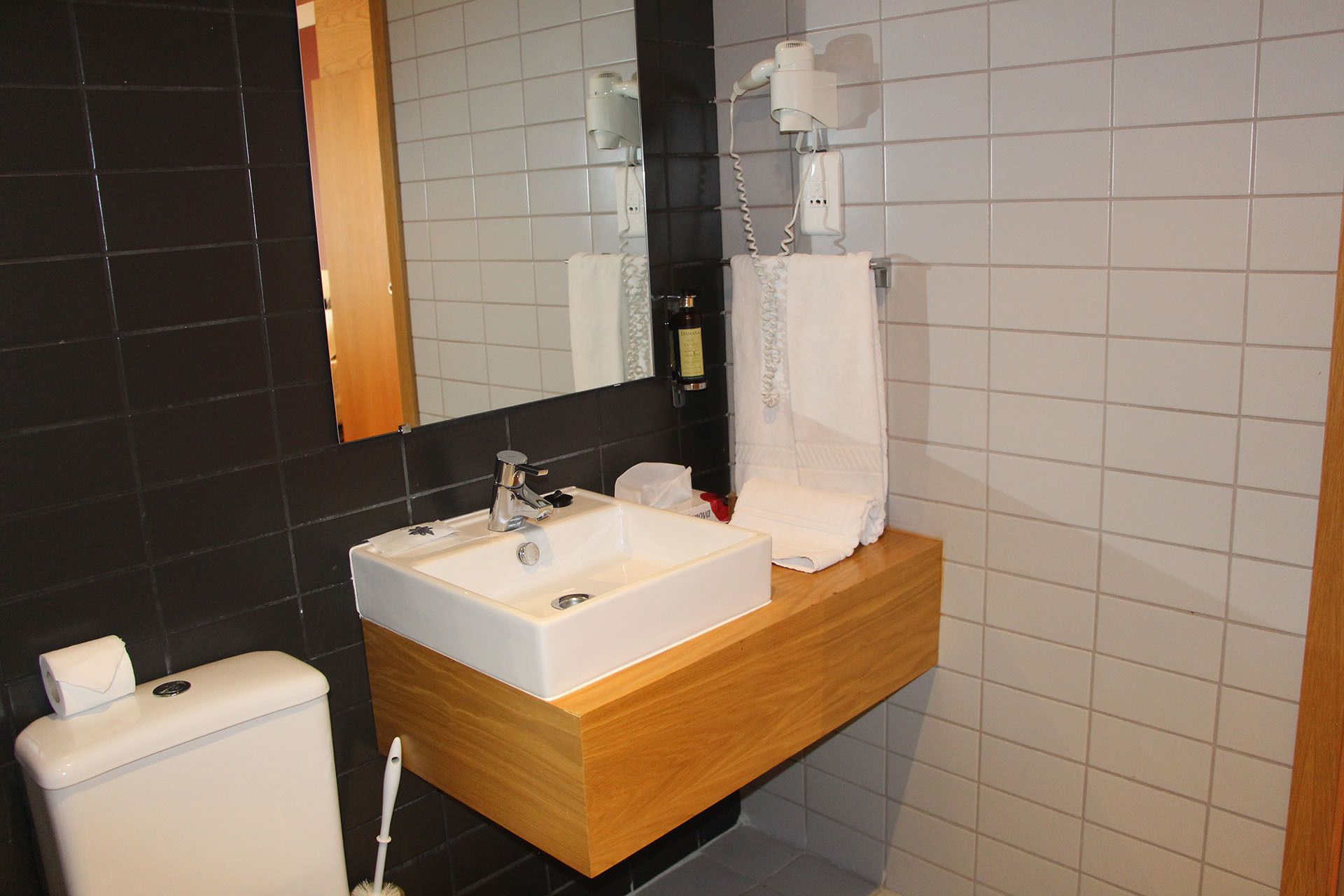A bathroom with a white sink, wooden vanity, a mirror, a hairdryer, and a toilet.