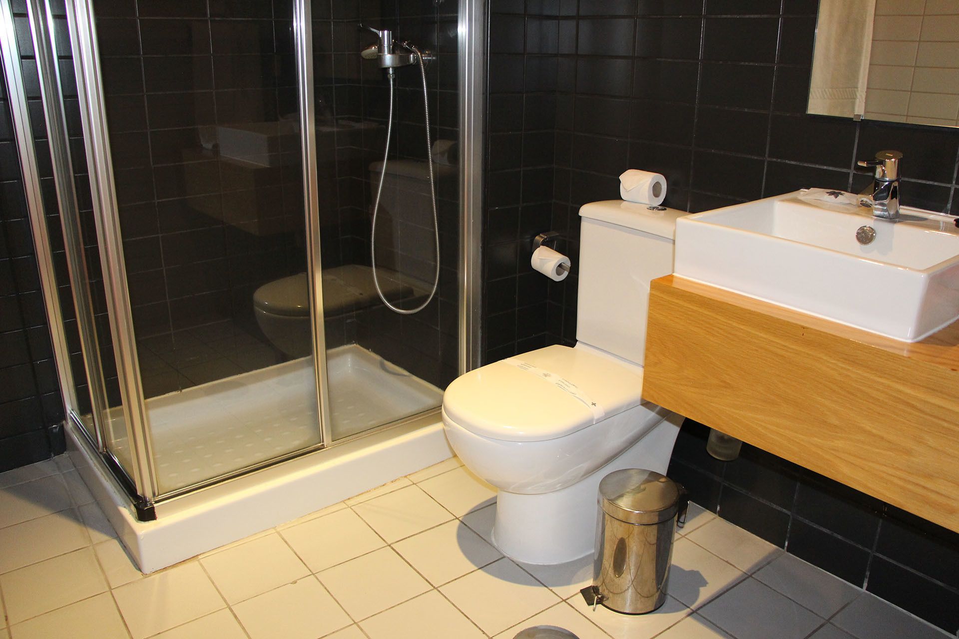 Un baño moderno con ducha de vidrio, inodoro blanco y tocador de madera con lavamanos.