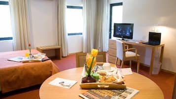 Une chambre d’hôtel avec un lit, un bureau équipé d’un ordinateur, une table à manger où le petit-déjeuner est servi, et de grandes fenêtres.