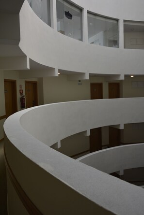 Ein mehrgeschossiges Interieur mit einem geschwungenen, weißen Balkonläufer, Holztüren und einem an der Wand befestigten Feuerlöscher.