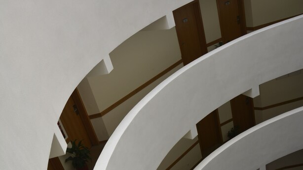 Ein mehrgeschossiges Interieur mit einem zentralen, offenen Bereich, umgeben von weißen Wänden und Holzböden.