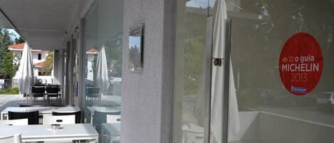 An outdoor seating area with tables and chairs, a glass wall with a Michelin logo, and a view of the surrounding area.