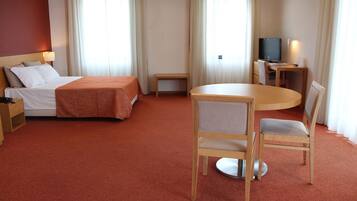 A hotel room with a bed, a round table with chairs, a TV, and a small table with a lamp.