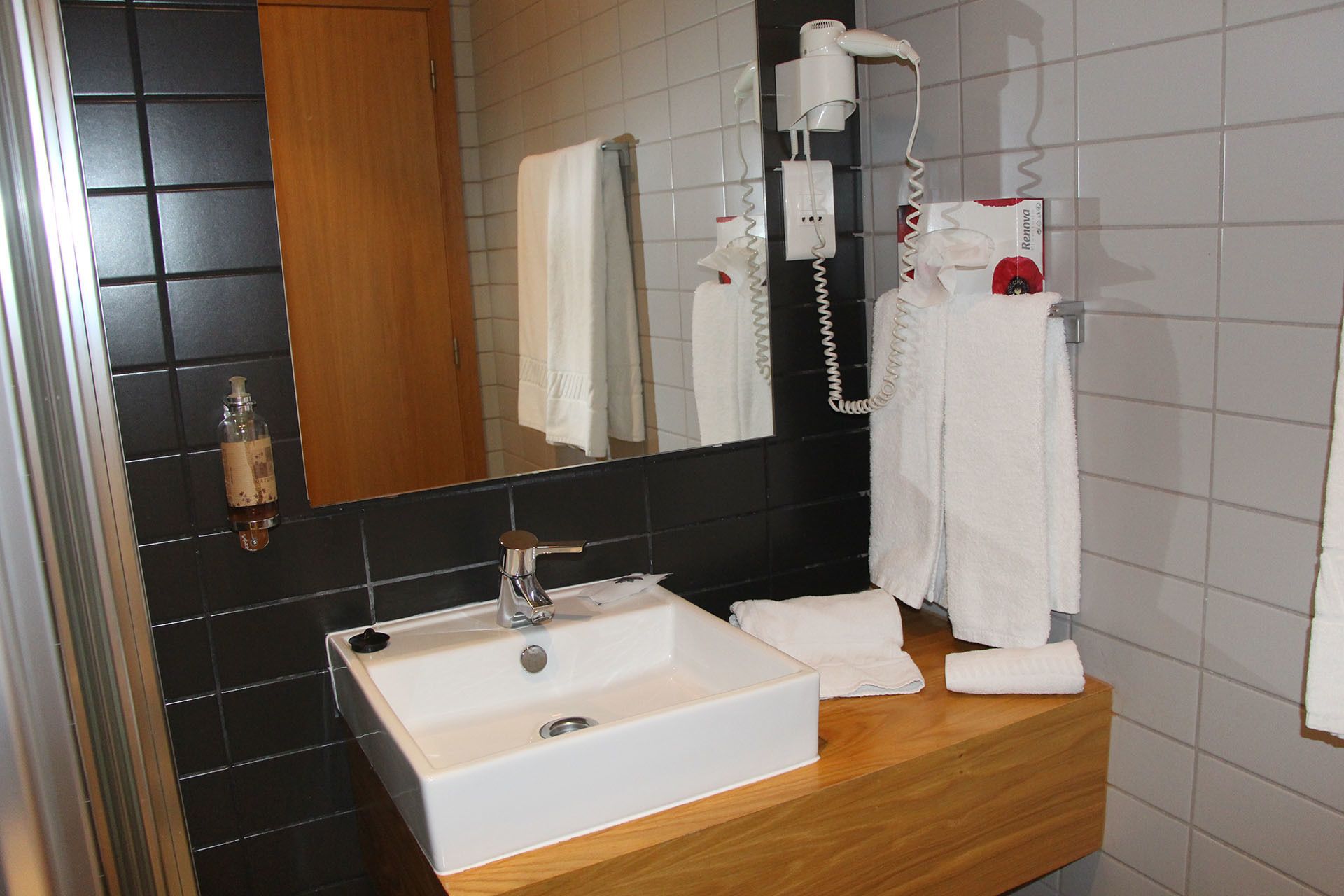 A bathroom with a white sink, black tiled walls, a wooden vanity, and a mirror.