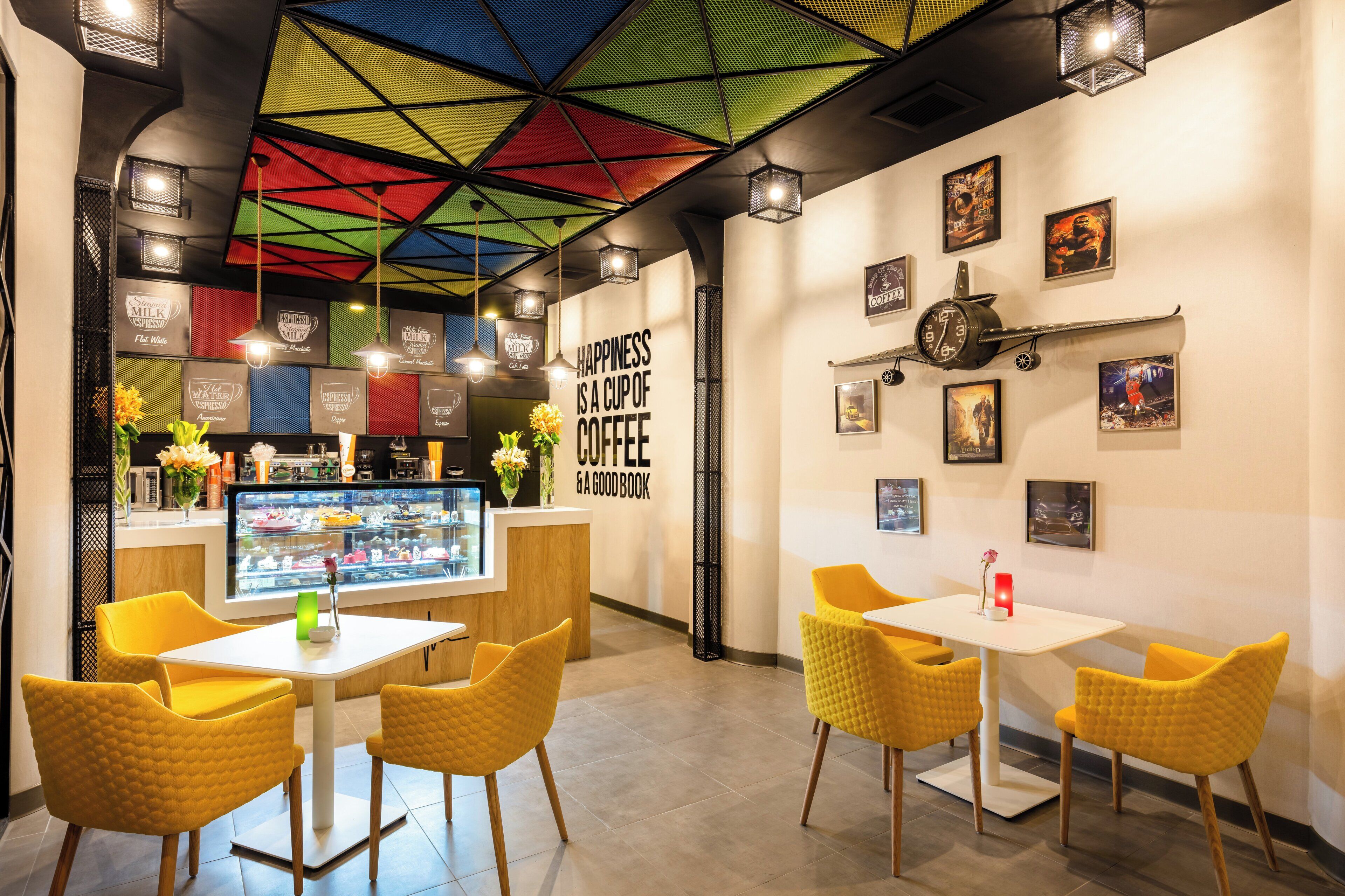 A cafe interior with yellow chairs, a coffee bar, and a colorful ceiling.