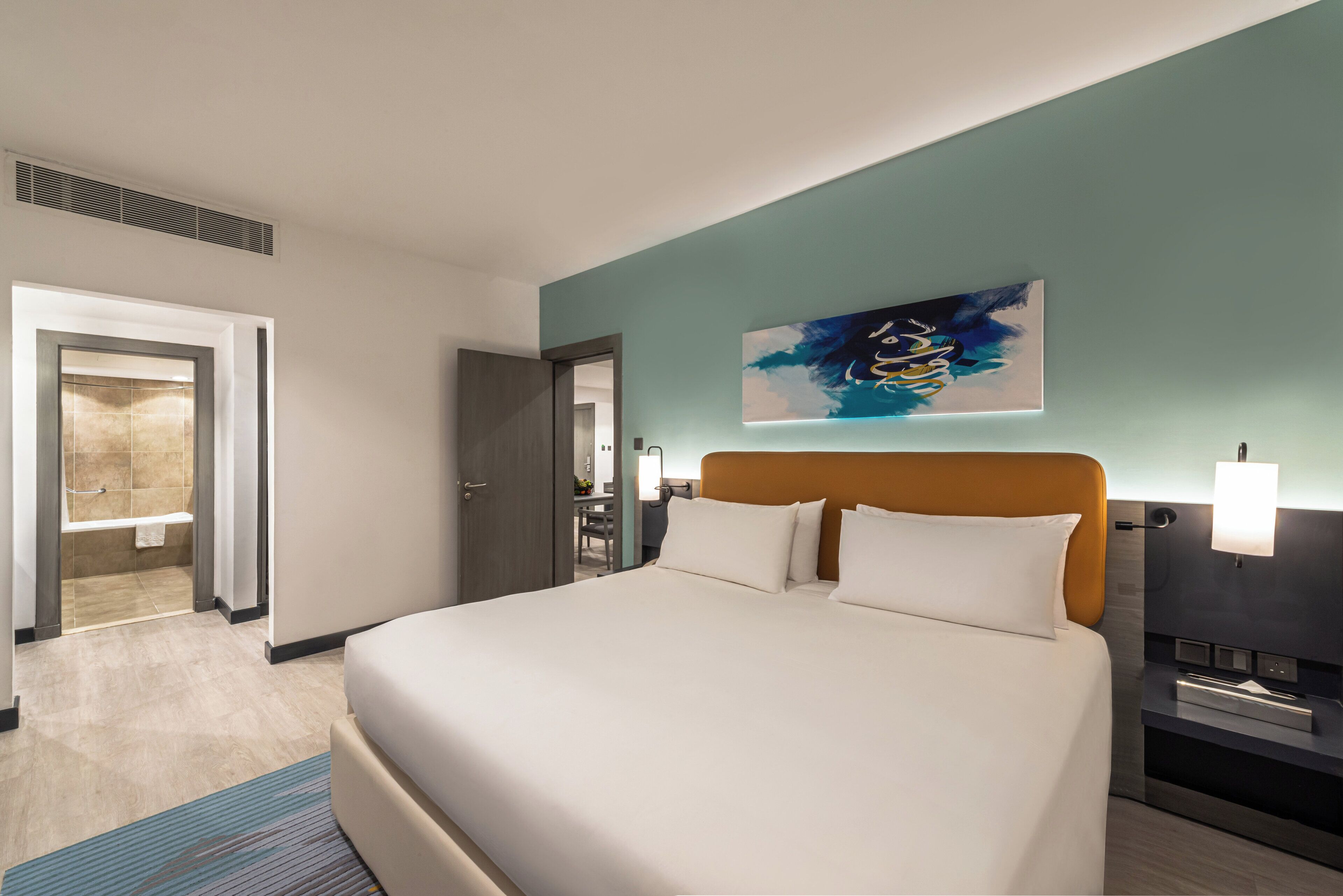 Una habitación de hotel con una cama grande, un baño con bañera y una puerta que da a otra habitación.
