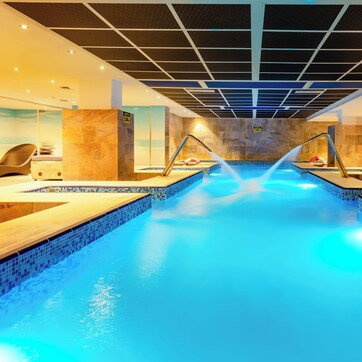Una piscina con borde de azulejos, un techo con diseño de cuadrícula y una pared con patrón de mosaicos.