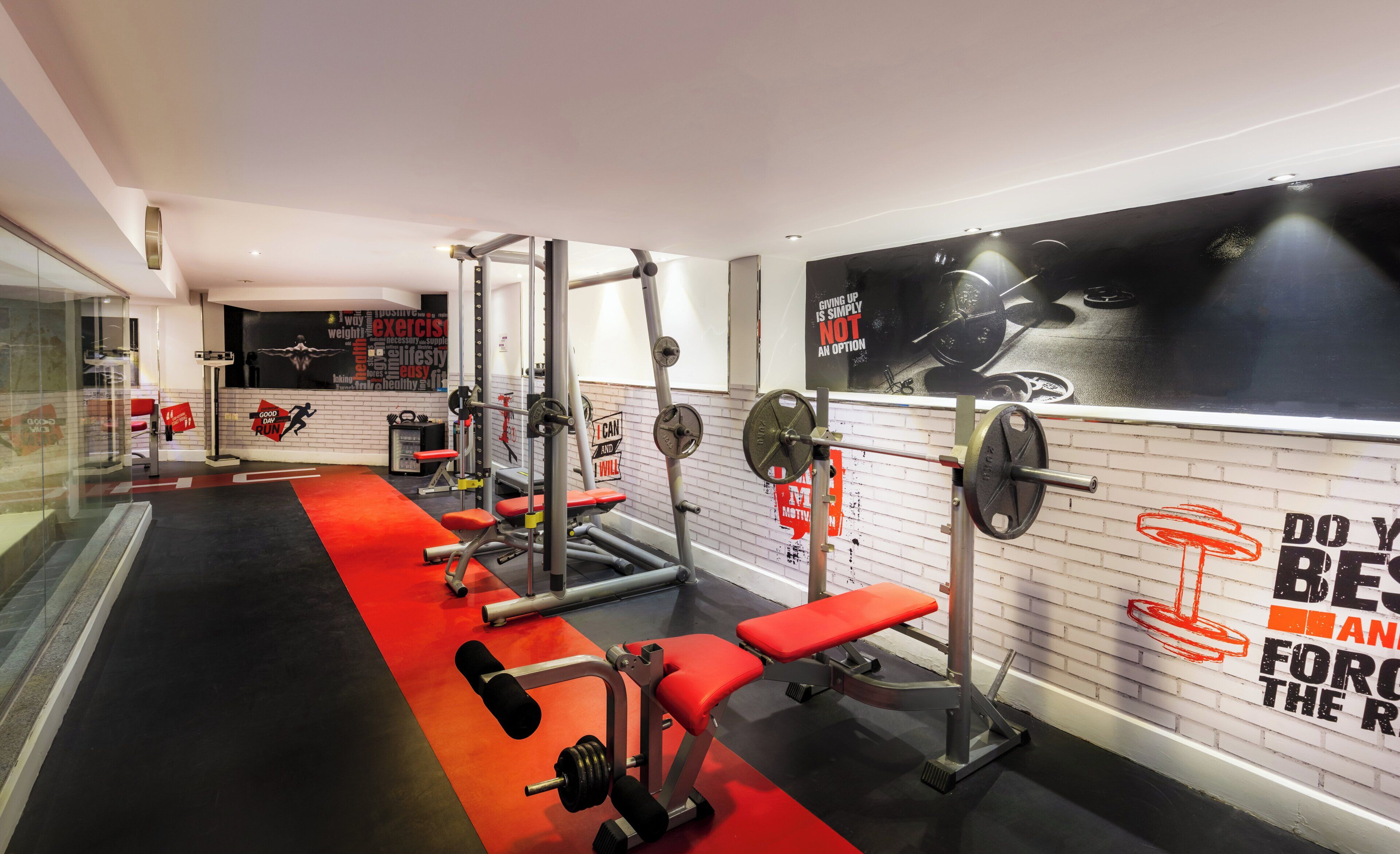 A gym with weightlifting equipment, a red bench, and motivational wall art.