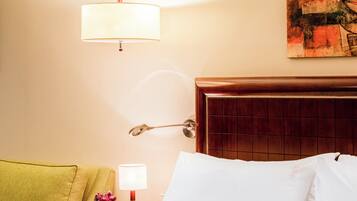 Habitación de hotel con cama, mesita de noche con lámpara, un cuadro en la pared y cabecero de madera.