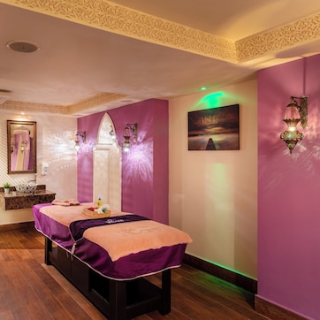 Un cuarto de spa con una camilla de masaje, un espejo, un lavamanos y una lámpara fijada a la pared.