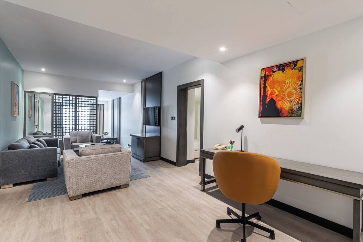 A modern living room with a sofa set, a desk with a chair, and a large painting on the wall.