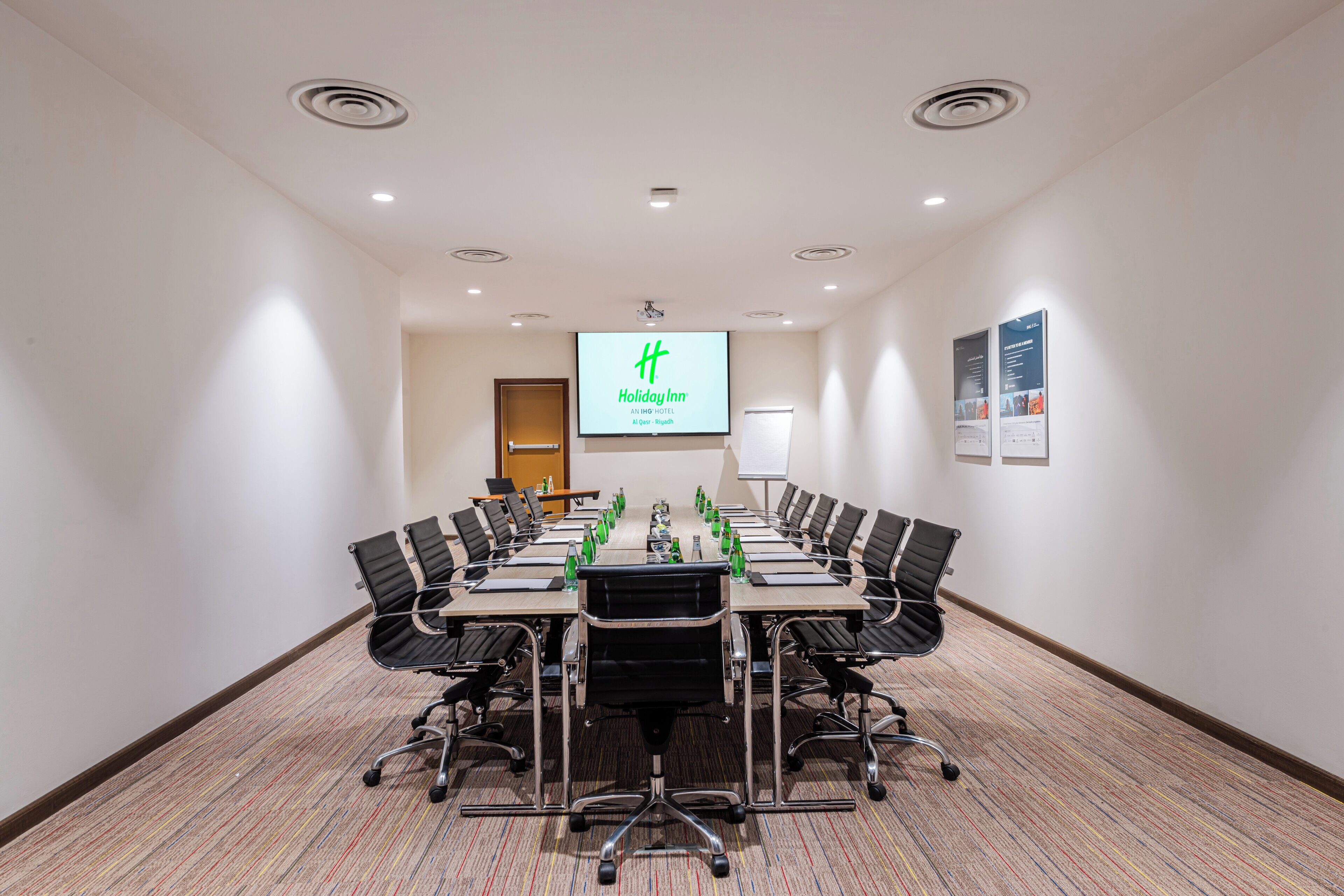Ein Konferenzraum mit langem Tisch, mehreren Stühlen, einer Projektionsleinwand und einer Tafel.