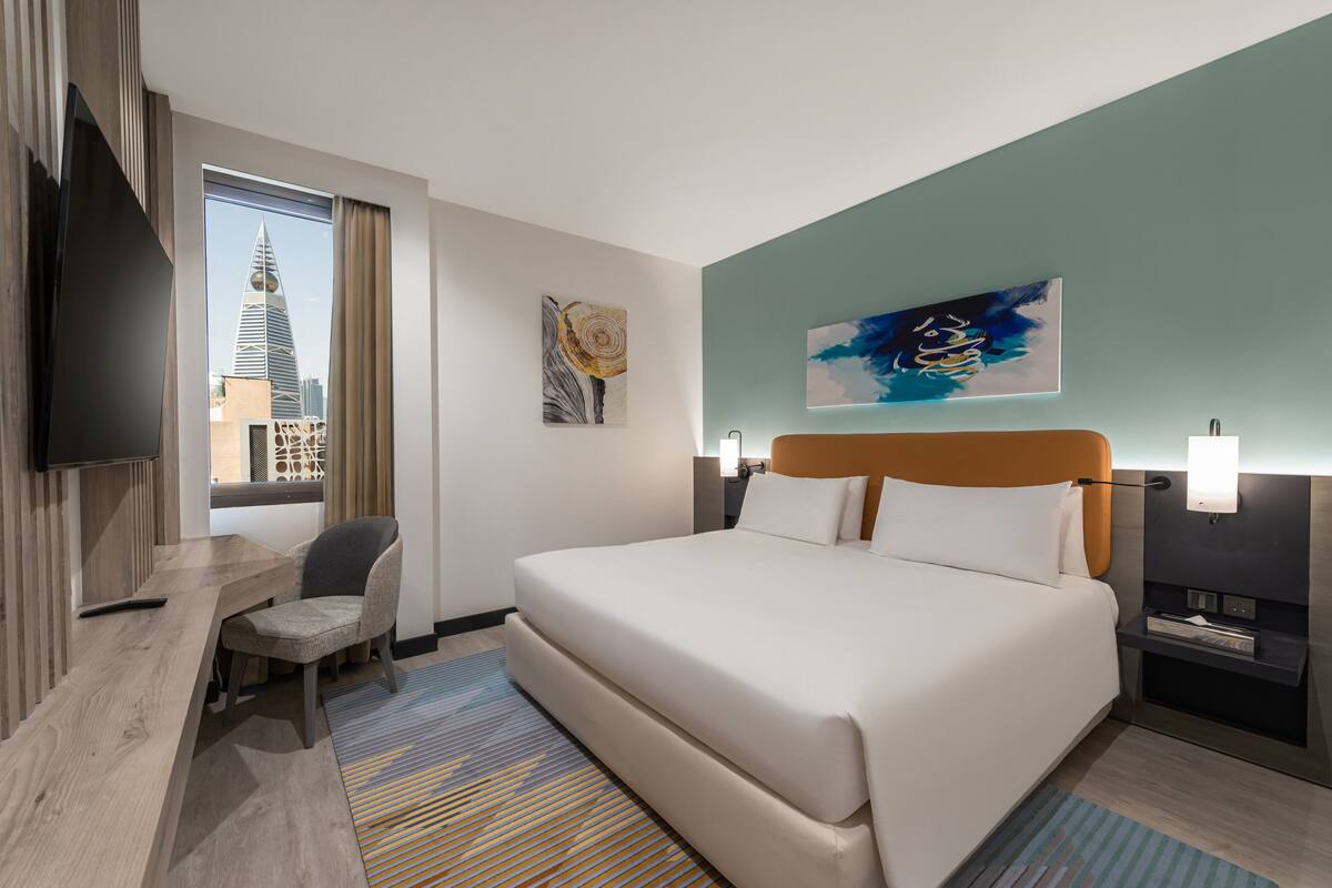 A hotel room with a bed, a desk, a chair, a TV, and a city view.