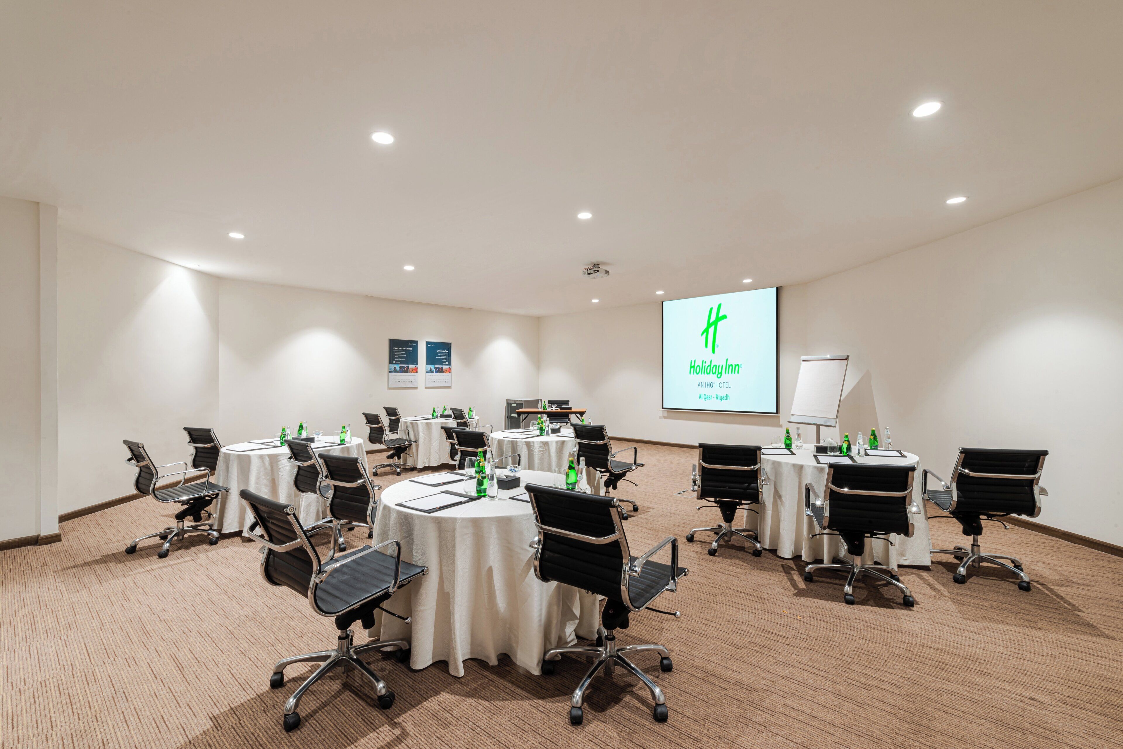 A conference room with round tables, black office chairs, and a projector screen displaying a presentation.