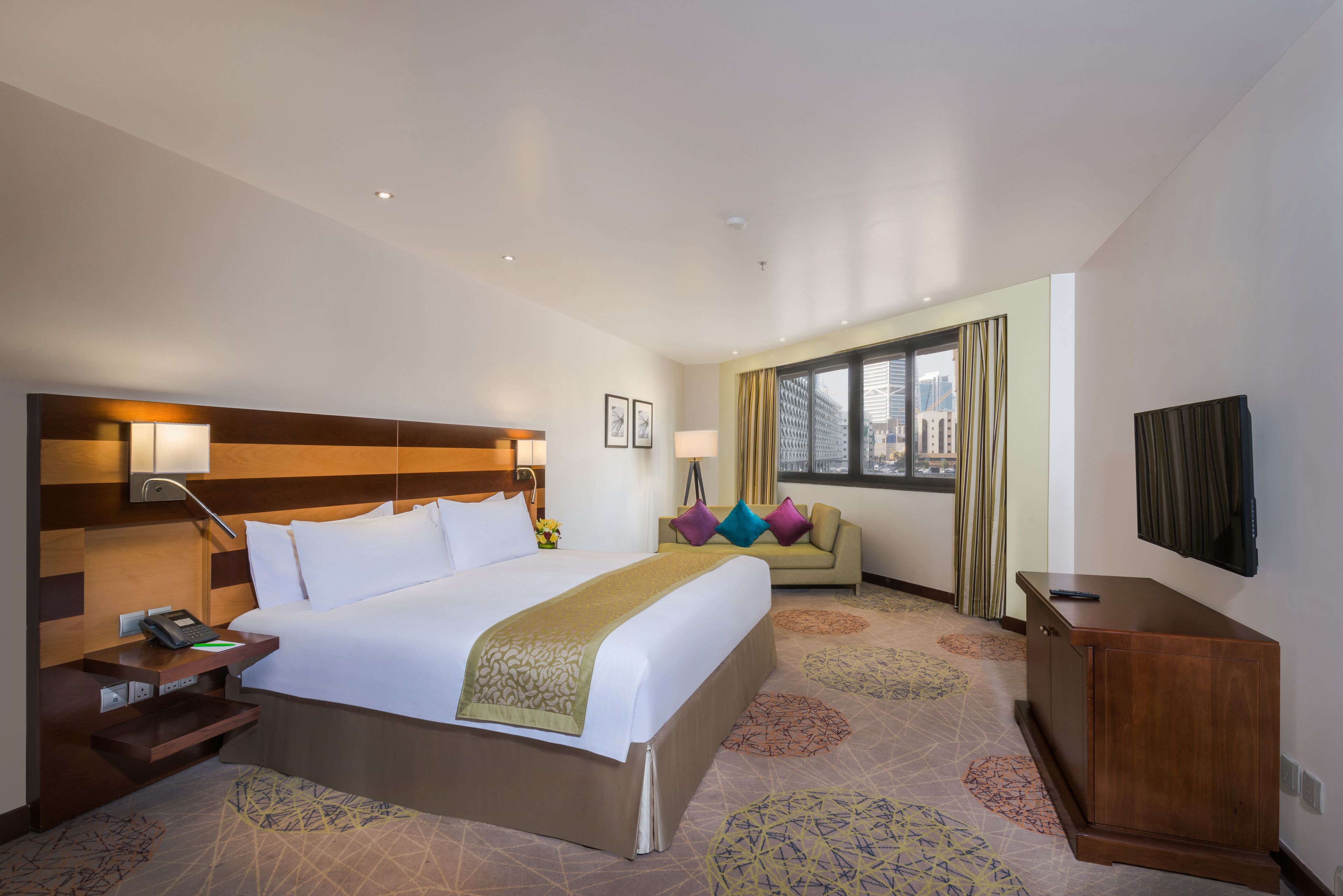 Habitación de hotel con una cama grande, mesitas de noche, un escritorio, un sofá y un televisor.