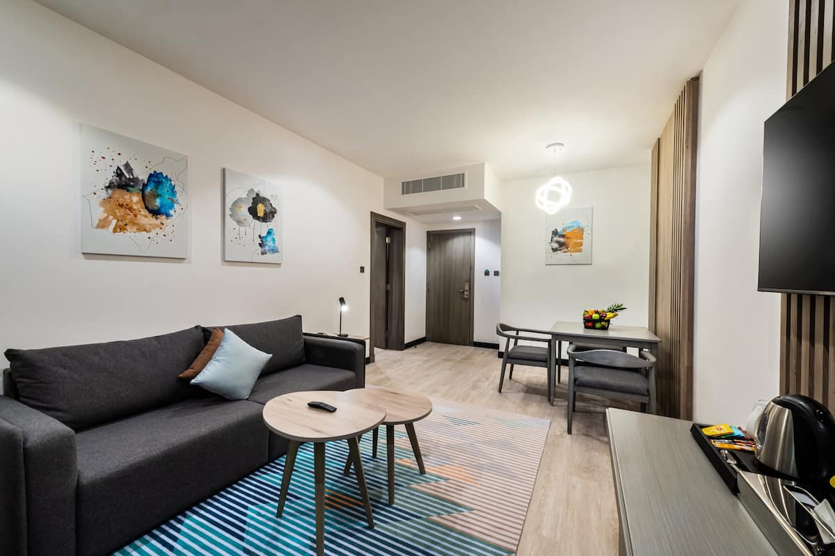 A modern hotel room with a sofa, a small table, a dining area with a table and chairs, and artwork on the walls.