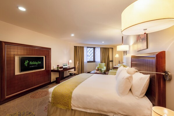 Quarto de hotel com cama, escrivaninha, cadeira, televisão e janela com cortinas.