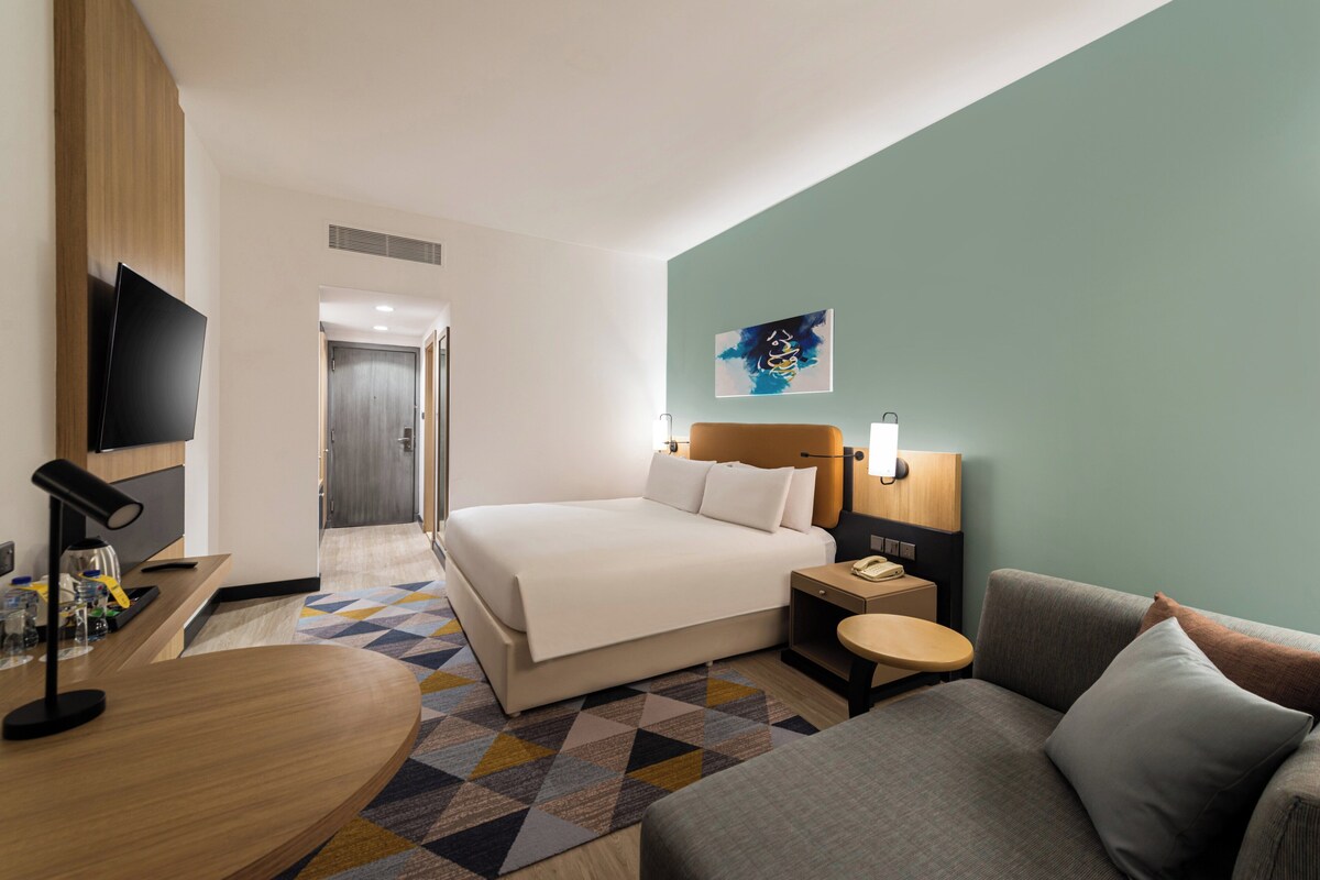 Een hotelkamer met een bed, een bureau, een televisie, een schilderij en een bank.