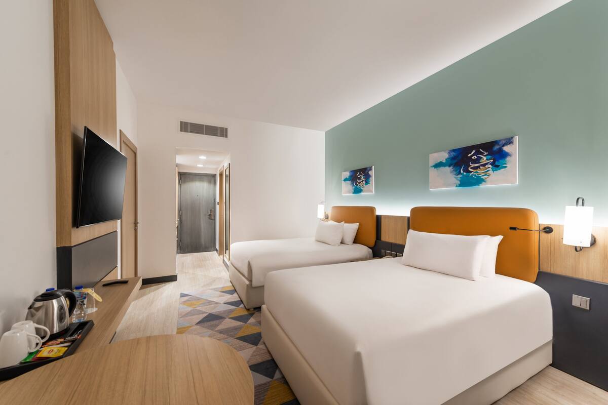A hotel room with two beds, a TV, artwork on the walls, and a coffee machine on the table.