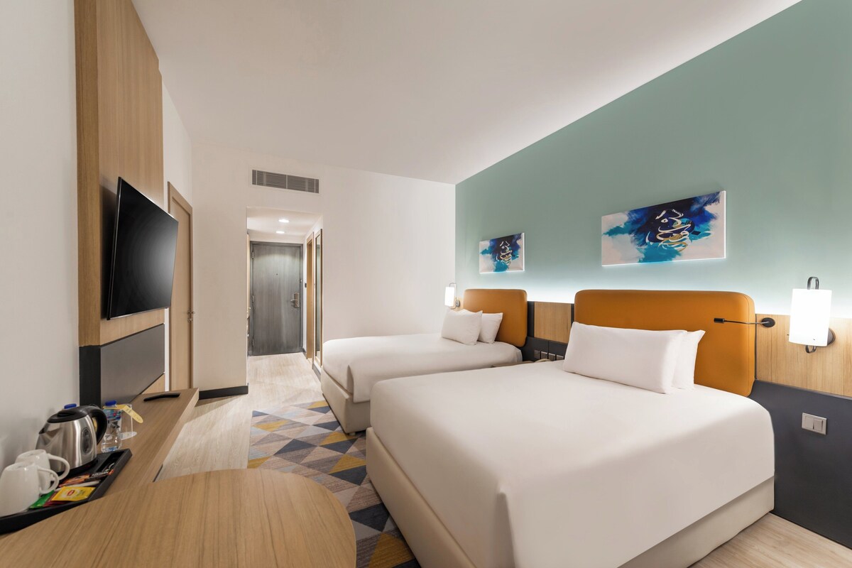 Een hotelkamer met twee bedden, een televisie, een bijzettafeltje en kunst aan de muren.