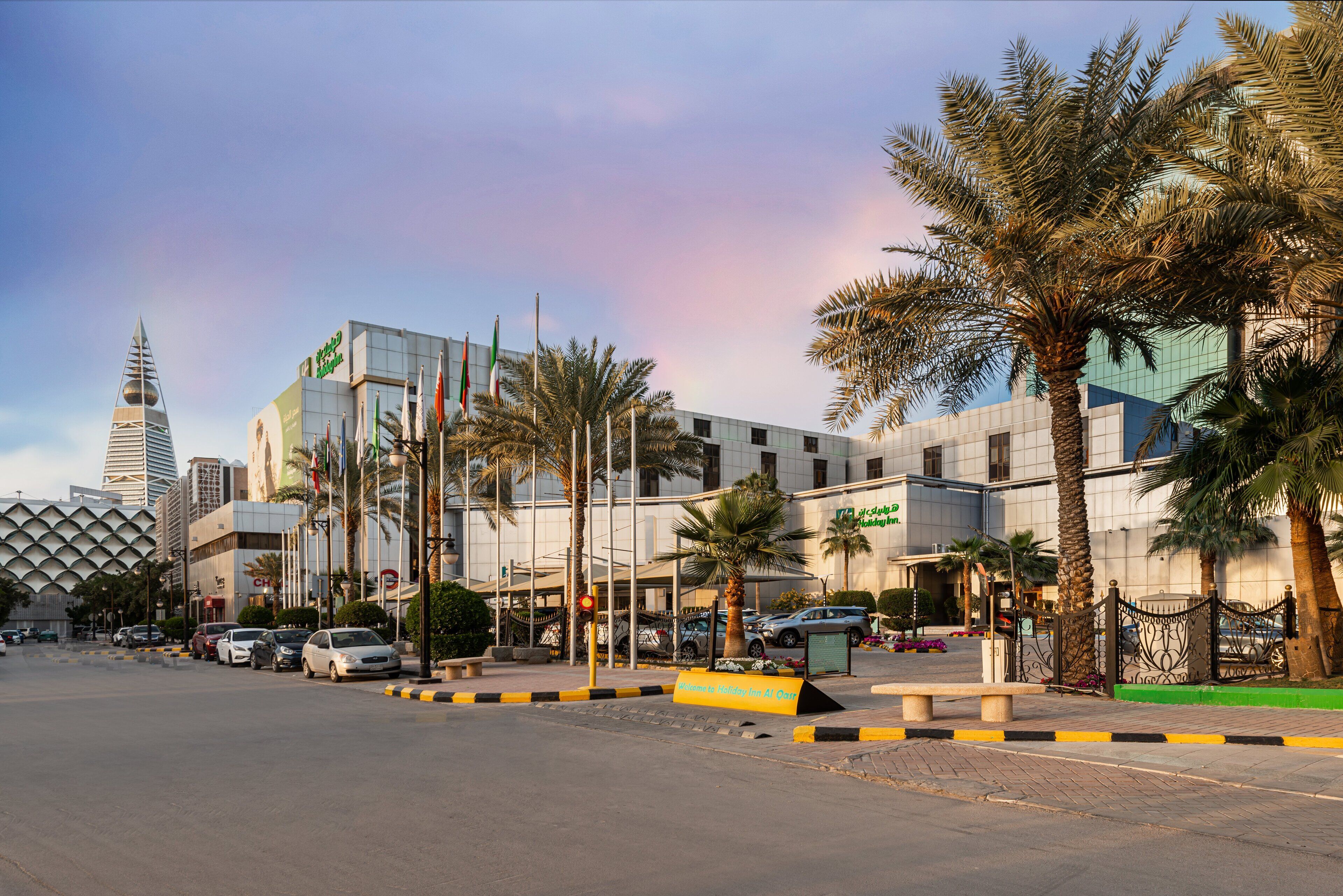 A modern building with a glass facade, palm trees, and a parking lot.
