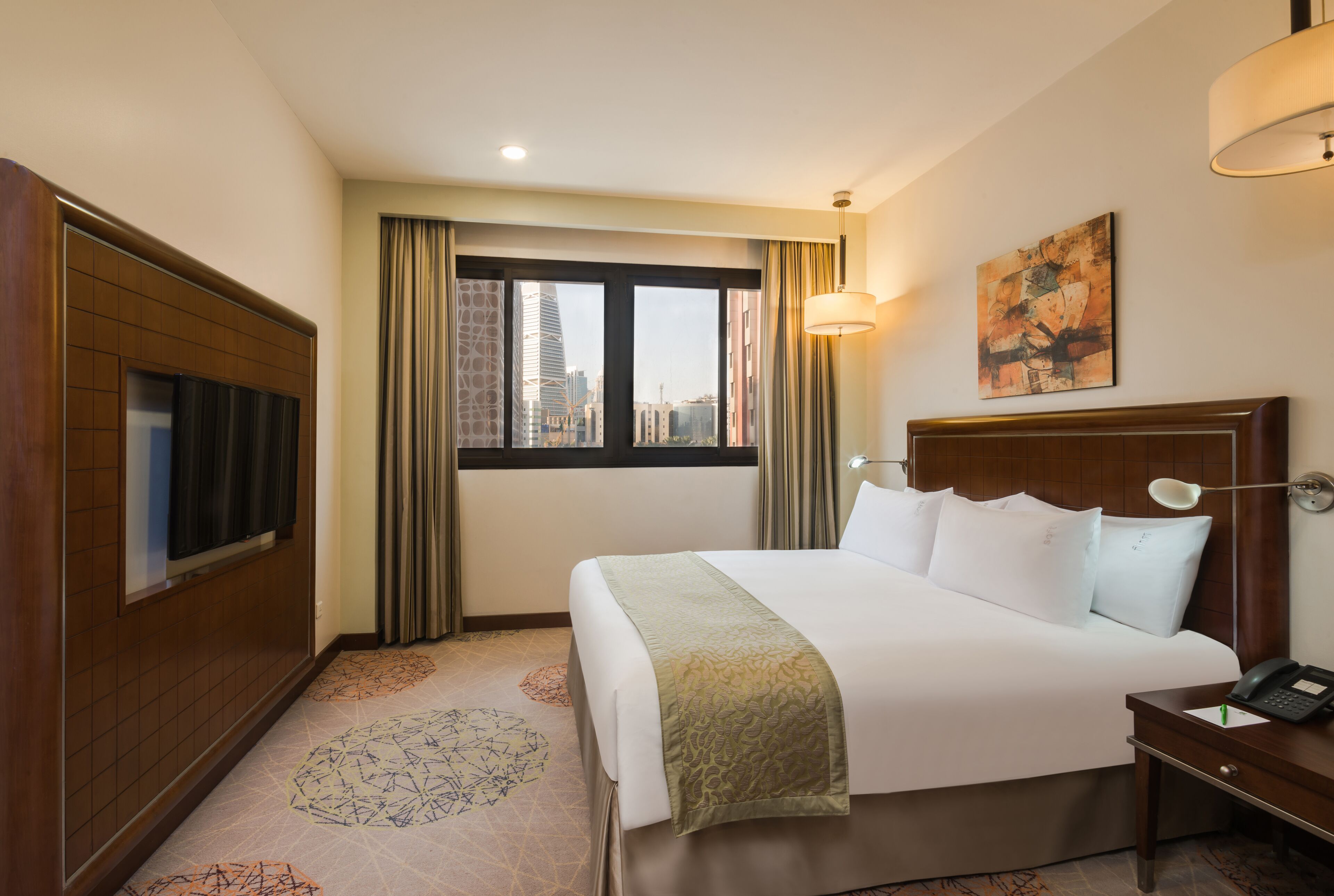 A hotel room with a large bed, a television, a desk with a telephone, and a window with curtains.