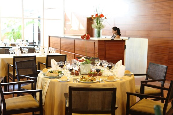 A restaurant with round tables set with plates, glasses, and cutlery. There is a vase with flowers on the counter.