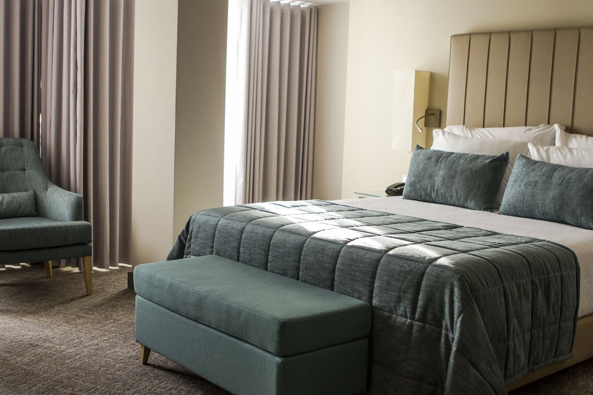 Une chambre d’hôtel avec un grand lit, un banc, une chaise et une table de chevet.