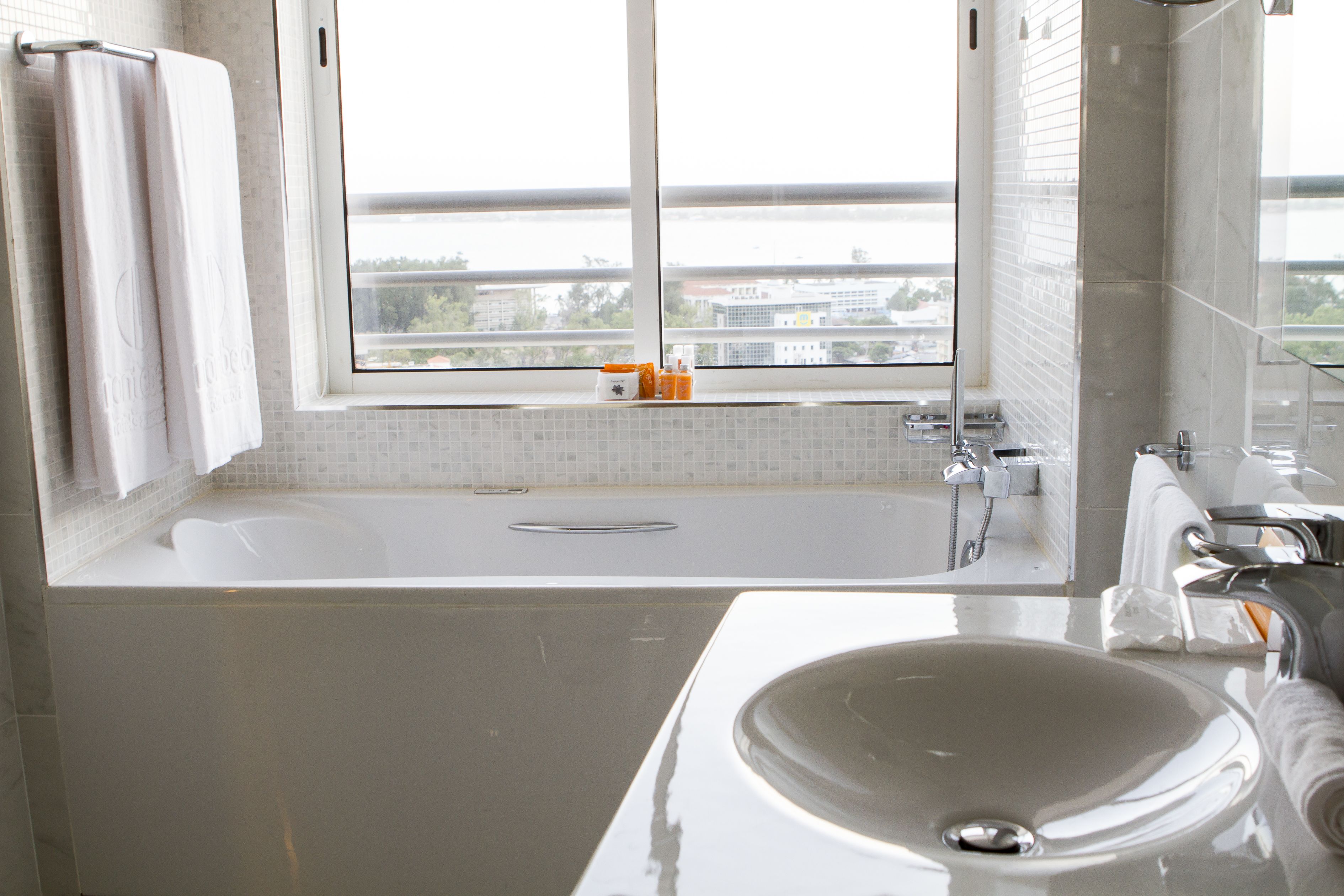 Un baño moderno con una bañera grande, un lavamanos y una ventana que ofrece vistas a edificios y un puente.