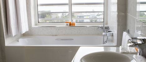 Un baño moderno con una bañera grande, un lavamanos y una ventana que ofrece vistas a edificios y un puente.