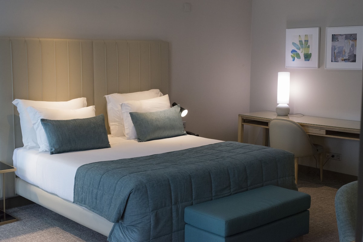 Une chambre d’hôtel bien rangée, avec un lit, une table de chevet, un bureau et une chaise.