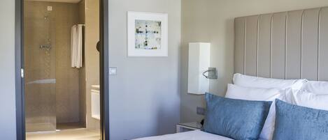 A hotel room with a bed, a nightstand, a wall-mounted lamp, a framed artwork, and a shower area.