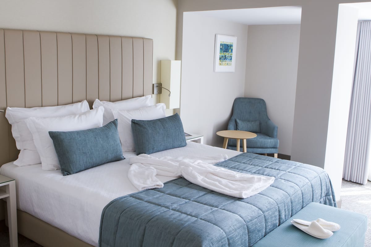 Une chambre d’hôtel avec un lit, une chaise, une petite table et une lampe fixée au mur.