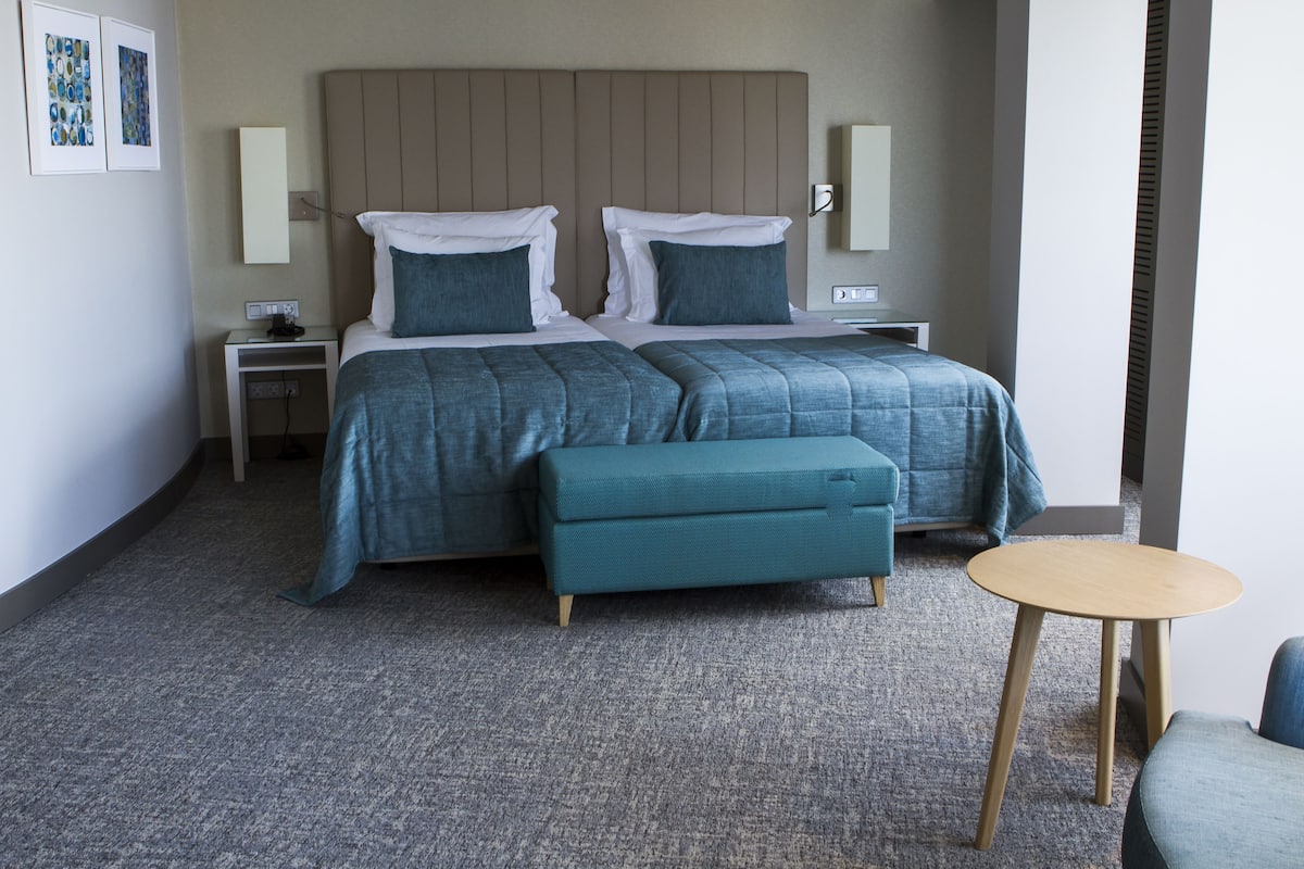 Une chambre d’hôtel avec un grand lit, deux tables de chevet, une petite table ronde et un banc.