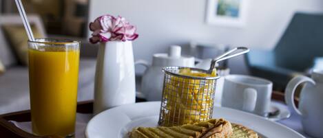 A breakfast tray with a glass of orange juice, a sandwich, a small salad, and a decorative flower.