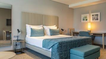 A modern hotel room with a large bed, bedside tables, a desk, a chair, and a small round table.