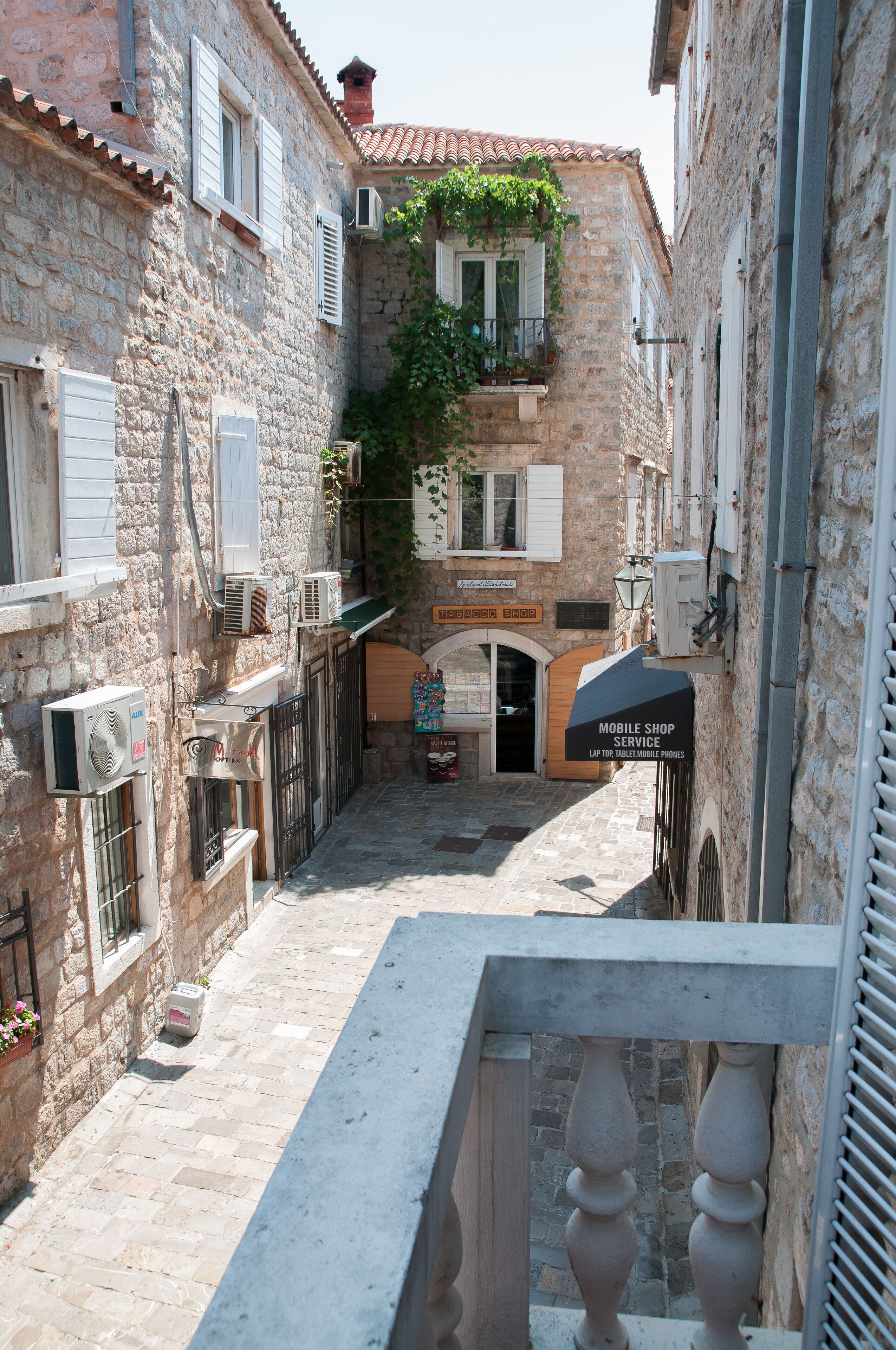 A narrow street with stone buildings, a shop with a sign for mobile shop service, and a small entrance.